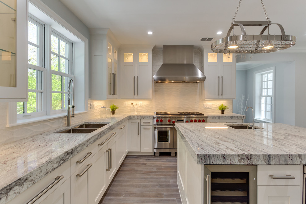 Inspiration for a large transitional l-shaped medium tone wood floor open concept kitchen remodel in DC Metro with a single-bowl sink, shaker cabinets, white cabinets, marble countertops, white backsplash, porcelain backsplash, stainless steel appliances and an island