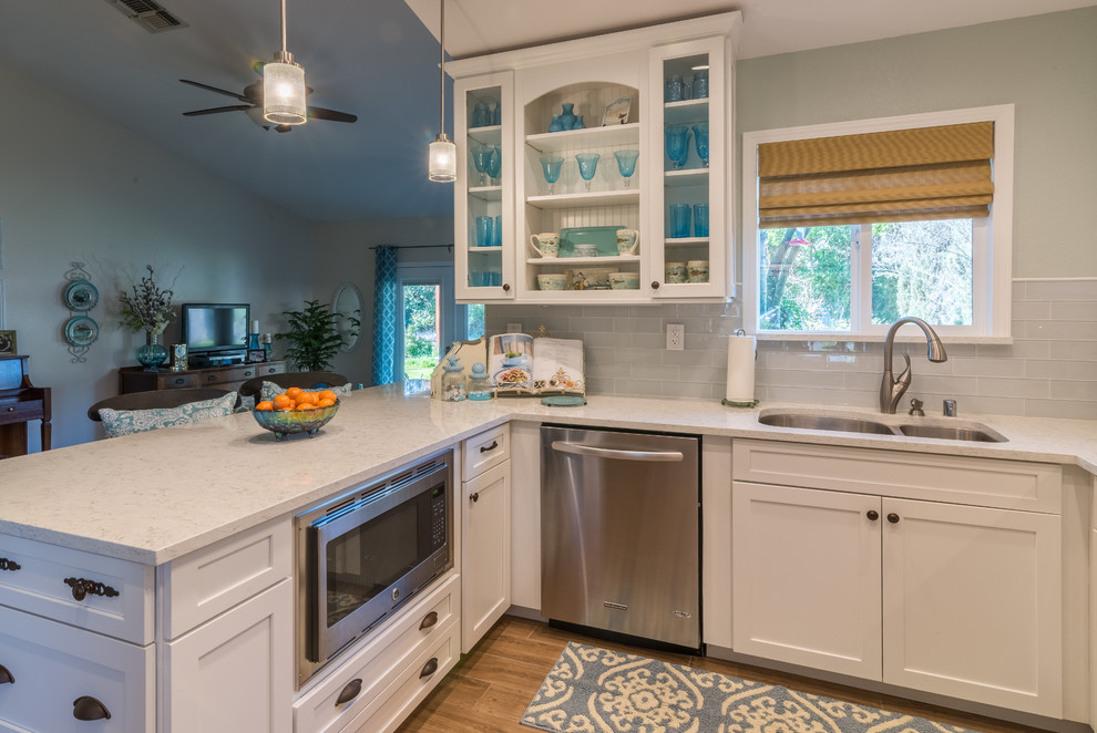 Inspiration for a mid-sized beach style u-shaped eat-in kitchen in Sacramento with an undermount sink, glass-front cabinets, white cabinets, marble benchtops, white splashback, glass tile splashback, stainless steel appliances, ceramic floors and a peninsula.