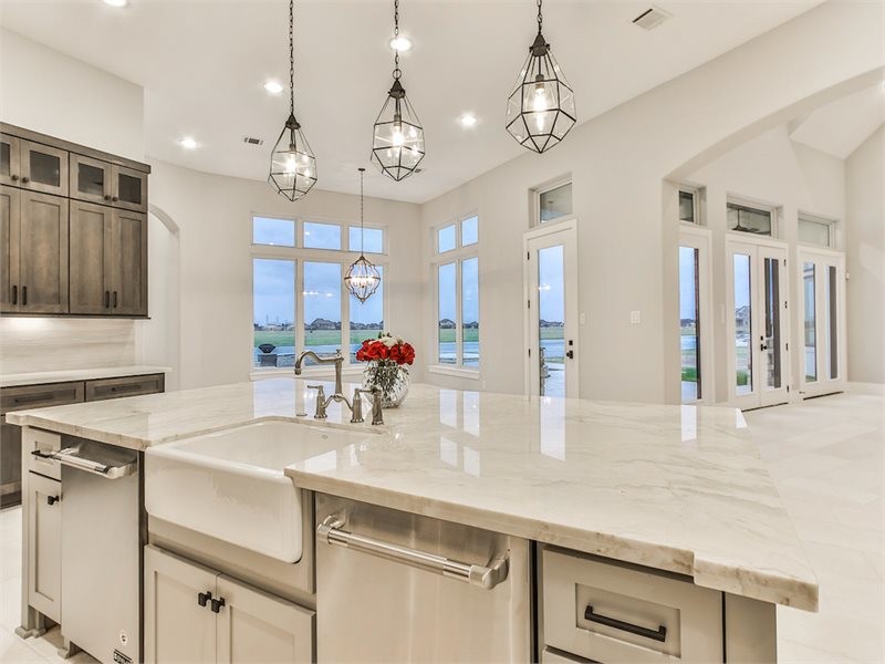Large transitional u-shaped eat-in kitchen in Houston with a farmhouse sink, recessed-panel cabinets, brown cabinets, marble benchtops, grey splashback, stainless steel appliances, limestone floors, with island and white floor.