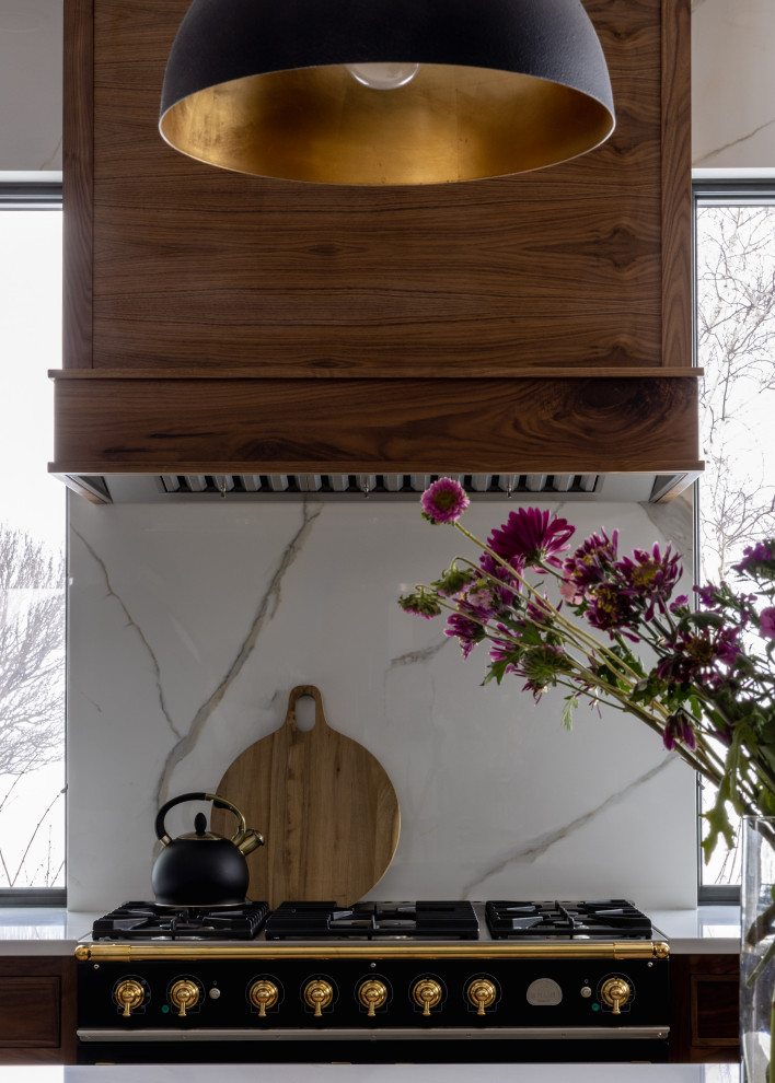 Mid-sized transitional l-shaped light wood floor and brown floor eat-in kitchen photo with a farmhouse sink, shaker cabinets, blue cabinets, quartz countertops, white backsplash, quartz backsplash, black appliances, an island and white countertops
