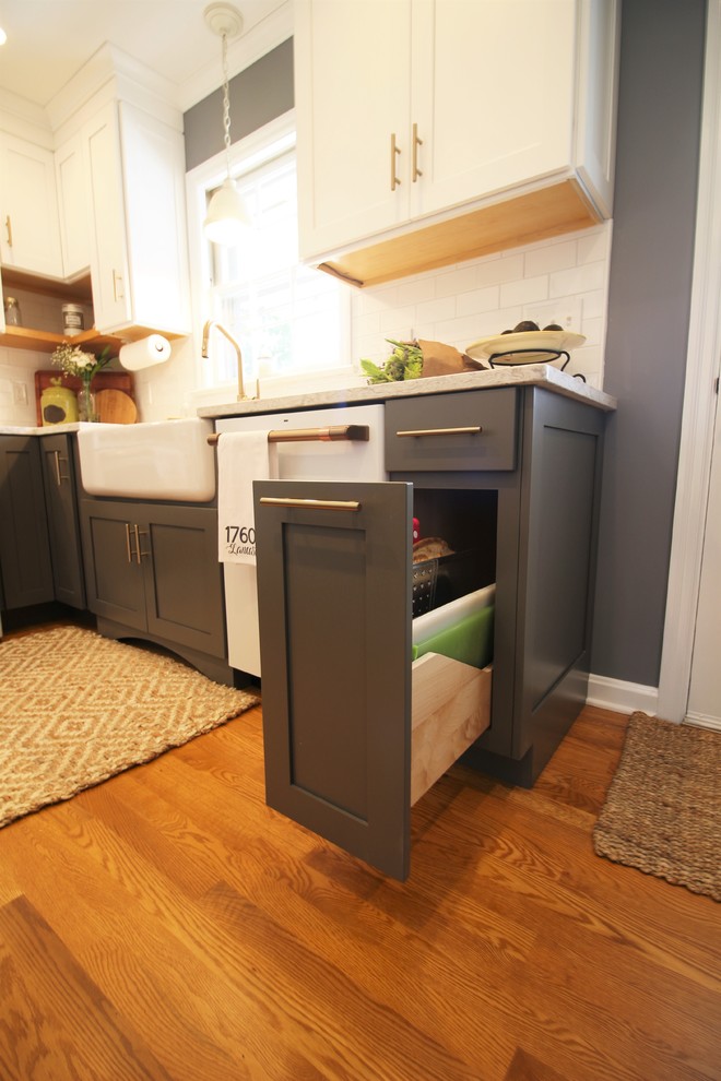 Example of a mid-sized transitional u-shaped medium tone wood floor and brown floor enclosed kitchen design with a farmhouse sink, shaker cabinets, white cabinets, quartz countertops, white backsplash, subway tile backsplash, white appliances, no island and beige countertops