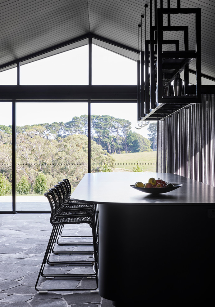 Large contemporary kitchen with black cabinets, granite benchtops, black splashback, glass sheet splashback, black appliances, with island, black benchtop and vaulted.