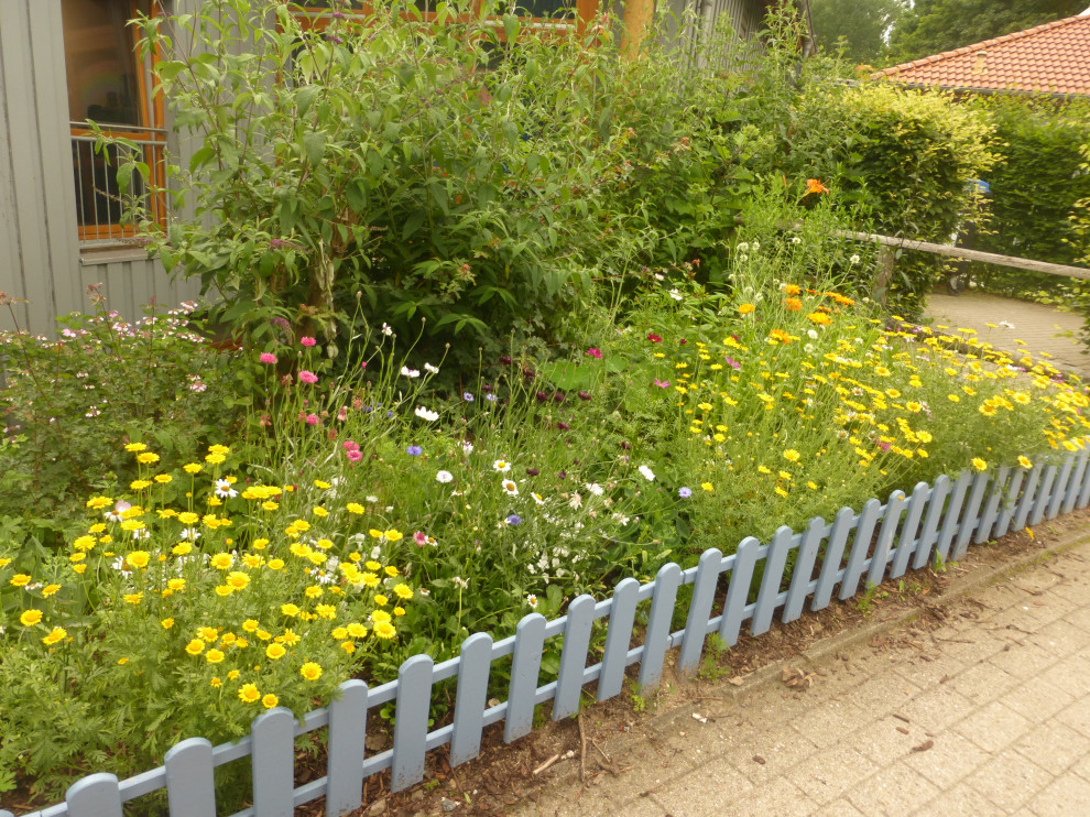 Aménagement d'un petit jardin latéral campagne l'été avec un massif de fleurs, une exposition ensoleillée et une clôture en bois.