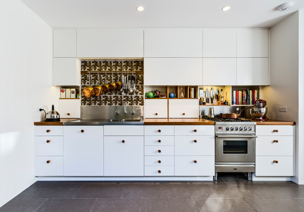 This is an example of a mid-sized contemporary galley kitchen in Sydney with flat-panel cabinets, white cabinets, wood benchtops, porcelain splashback, stainless steel appliances, a double-bowl sink, metallic splashback, ceramic floors, grey floor and brown benchtop.