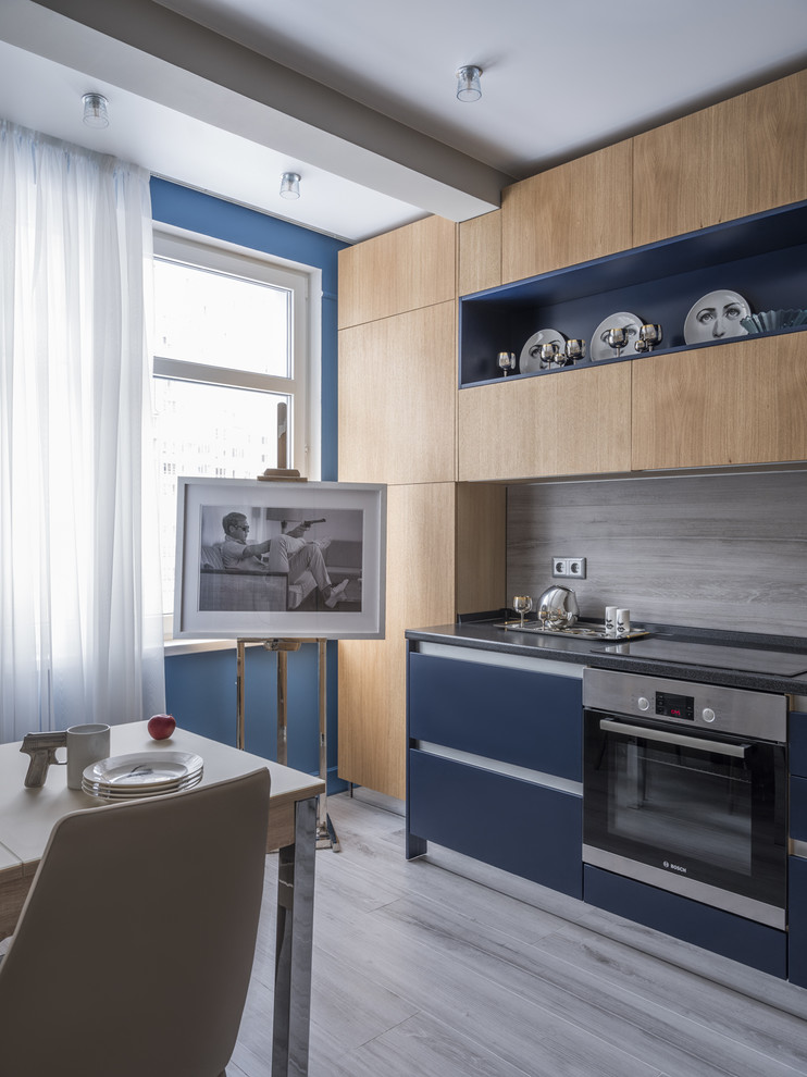 This is an example of a contemporary single-wall separate kitchen in Moscow with flat-panel cabinets, blue cabinets, grey splashback, stainless steel appliances, no island, grey floor and black benchtop.