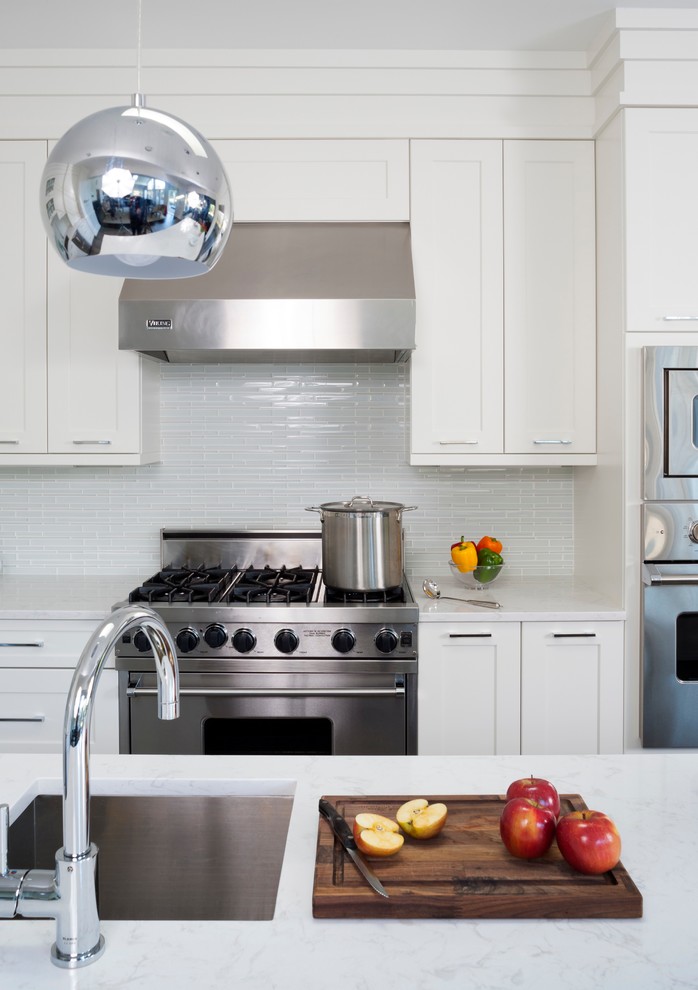 Enclosed kitchen - mid-sized transitional l-shaped ceramic tile and brown floor enclosed kitchen idea in DC Metro with an undermount sink, shaker cabinets, white cabinets, quartz countertops, white backsplash, glass tile backsplash, stainless steel appliances and an island
