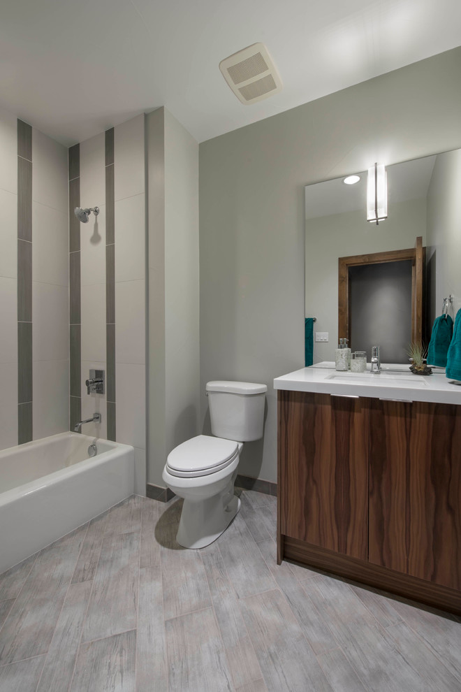 This is an example of a small contemporary bathroom in Denver with an undermount sink, flat-panel cabinets, medium wood cabinets, engineered quartz benchtops, an alcove tub, a shower/bathtub combo, a one-piece toilet, gray tile, ceramic tile, grey walls and porcelain floors.