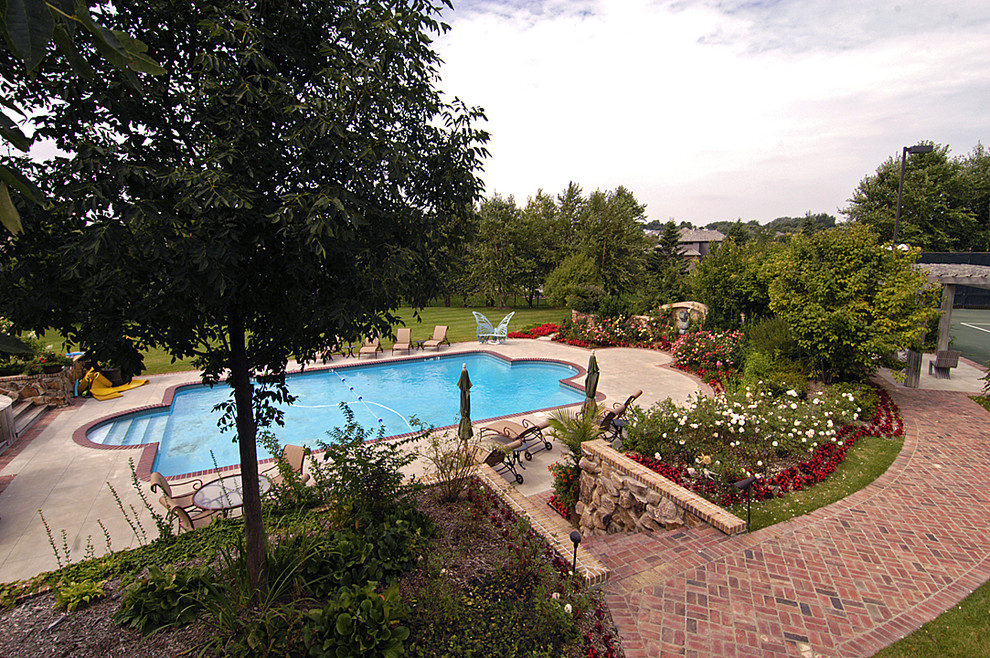 Expansive country backyard custom-shaped lap pool in Omaha with brick pavers.