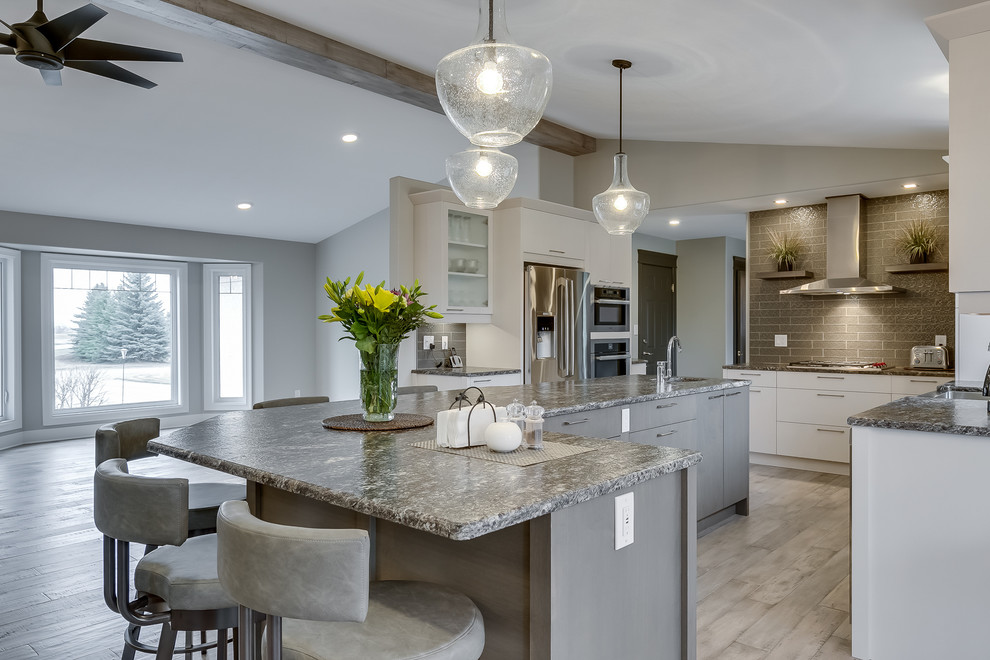 Eat-in kitchen - large transitional l-shaped light wood floor eat-in kitchen idea with flat-panel cabinets, an island, white cabinets, gray backsplash, subway tile backsplash and stainless steel appliances