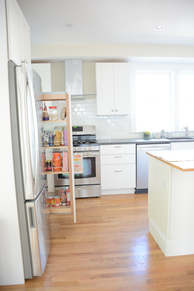 Inspiration for a large transitional l-shaped medium tone wood floor and brown floor kitchen pantry remodel in Boston with a drop-in sink, flat-panel cabinets, white cabinets, solid surface countertops, white backsplash, subway tile backsplash, stainless steel appliances and an island