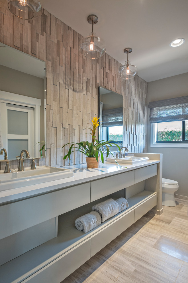 Bathroom - mid-sized transitional 3/4 gray tile porcelain tile and double-sink bathroom idea with flat-panel cabinets, white cabinets, a one-piece toilet, beige walls, a drop-in sink, solid surface countertops and white countertops