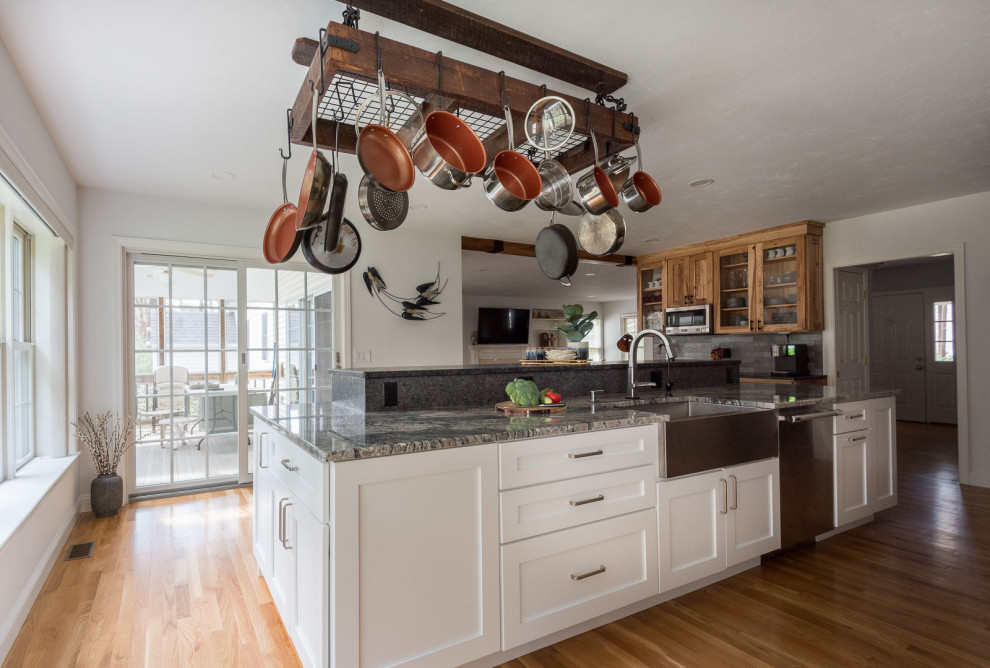Example of a large transitional single-wall light wood floor and brown floor eat-in kitchen design in Boston with a farmhouse sink, shaker cabinets, white cabinets, granite countertops, gray backsplash, ceramic backsplash, stainless steel appliances, an island and gray countertops