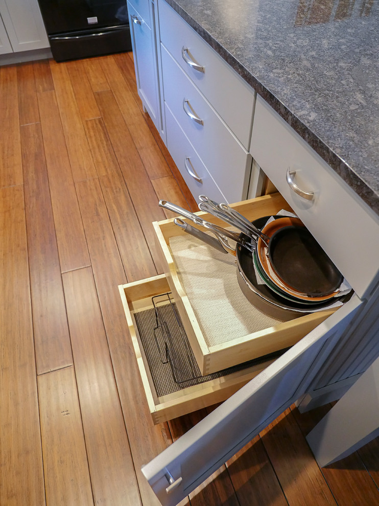 Large transitional l-shaped bamboo floor eat-in kitchen photo in Burlington with a farmhouse sink, shaker cabinets, gray cabinets, granite countertops, gray backsplash, stone tile backsplash, black appliances and an island