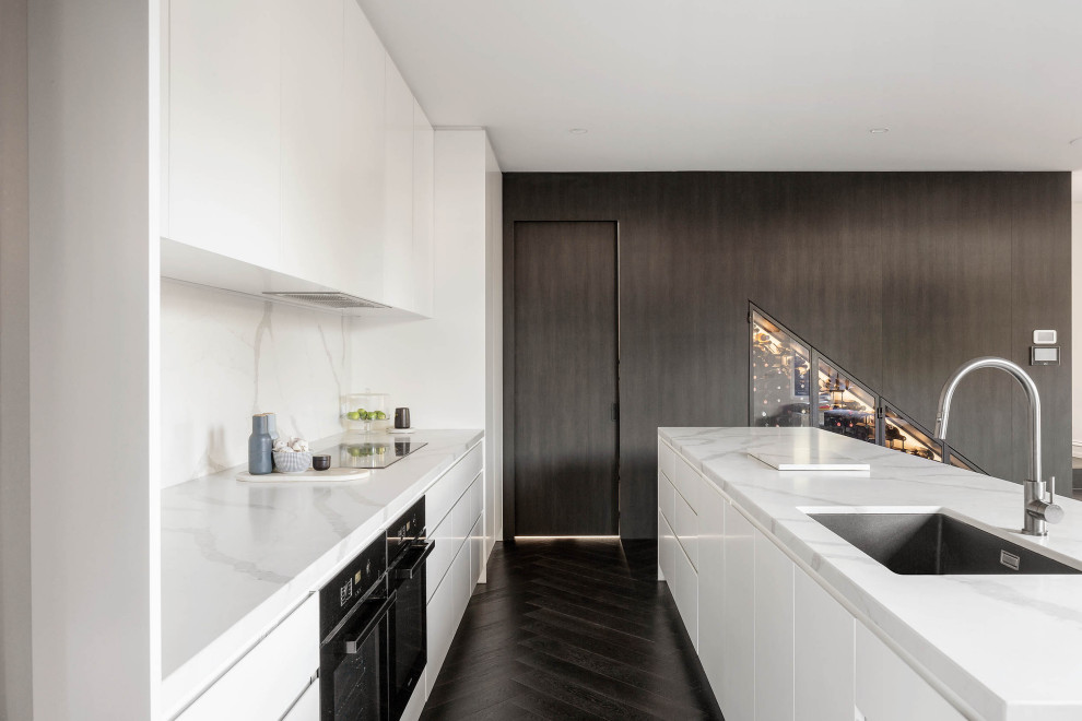 This is an example of a large contemporary u-shaped open plan kitchen in Melbourne with an undermount sink, flat-panel cabinets, white cabinets, quartz benchtops, white splashback, engineered quartz splashback, black appliances, dark hardwood floors, with island, black floor and white benchtop.