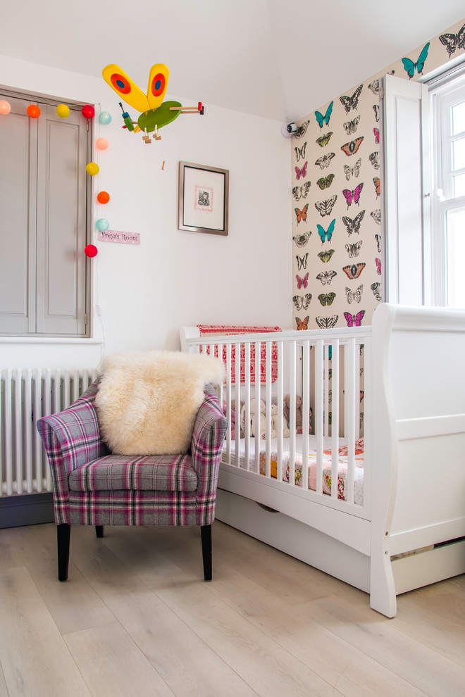 Mid-sized traditional nursery in London with white walls, light hardwood floors and beige floor for girls.