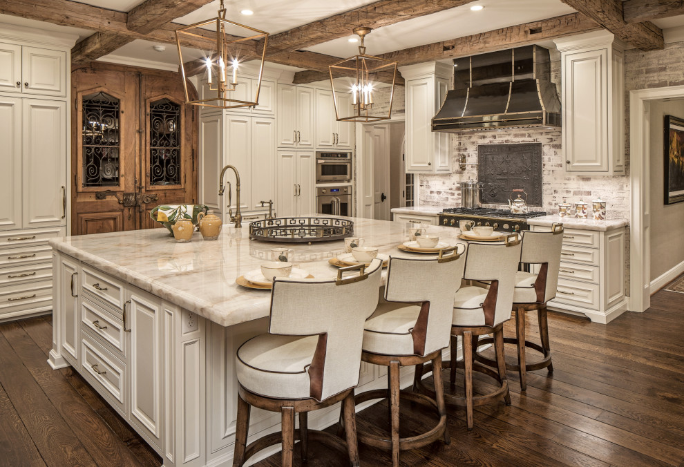 Inspiration for an expansive traditional l-shaped kitchen in Omaha with a farmhouse sink, raised-panel cabinets, white cabinets, granite benchtops, white splashback, brick splashback, stainless steel appliances, medium hardwood floors, with island, brown floor and beige benchtop.