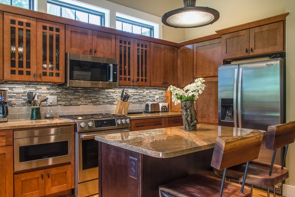 Example of a mid-sized transitional l-shaped medium tone wood floor and brown floor eat-in kitchen design with shaker cabinets, medium tone wood cabinets, granite countertops, brown backsplash, glass tile backsplash, stainless steel appliances, an island and a farmhouse sink