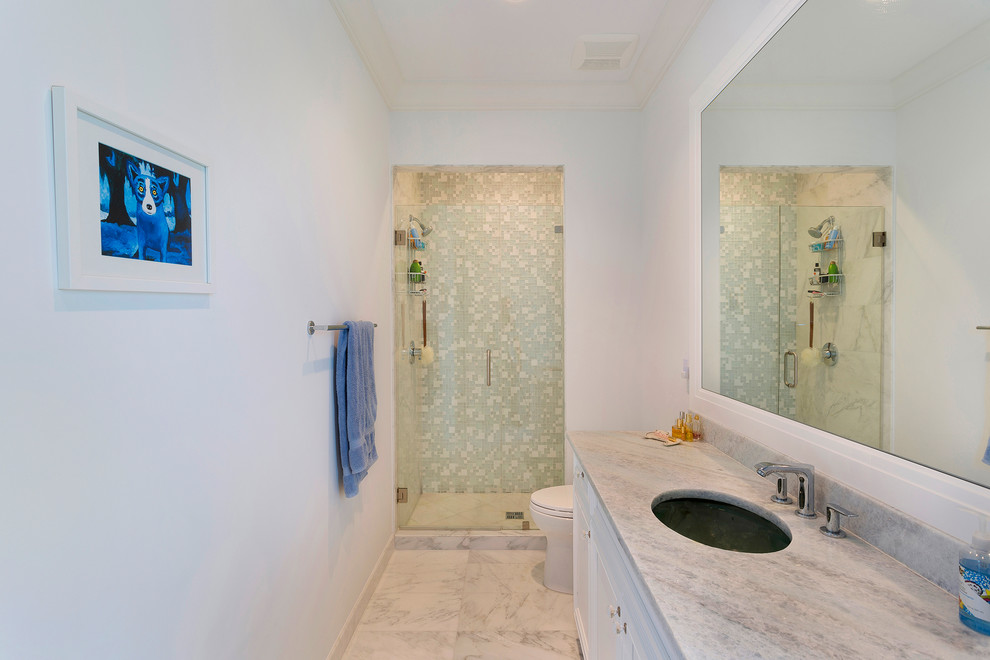 This is an example of an expansive tropical kids bathroom in Other with recessed-panel cabinets, white cabinets, an alcove shower, a one-piece toilet, gray tile, marble, white walls, marble floors, an undermount sink, marble benchtops, grey floor, a hinged shower door and grey benchtops.