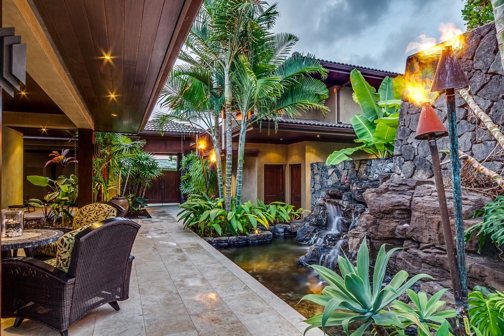Design ideas for an expansive tropical side yard patio in Hawaii with a water feature, tile and a roof extension.