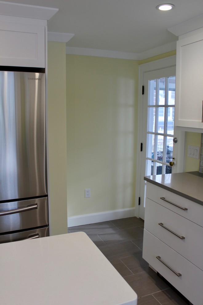 Eat-in kitchen - mid-sized transitional l-shaped porcelain tile and gray floor eat-in kitchen idea in Boston with a farmhouse sink, shaker cabinets, white cabinets, quartz countertops, gray backsplash, mosaic tile backsplash, stainless steel appliances and an island