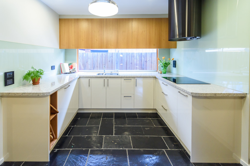 Photo of a mid-sized modern u-shaped open plan kitchen in Melbourne with a drop-in sink, flat-panel cabinets, light wood cabinets, laminate benchtops, blue splashback, glass tile splashback, black appliances, slate floors and a peninsula.