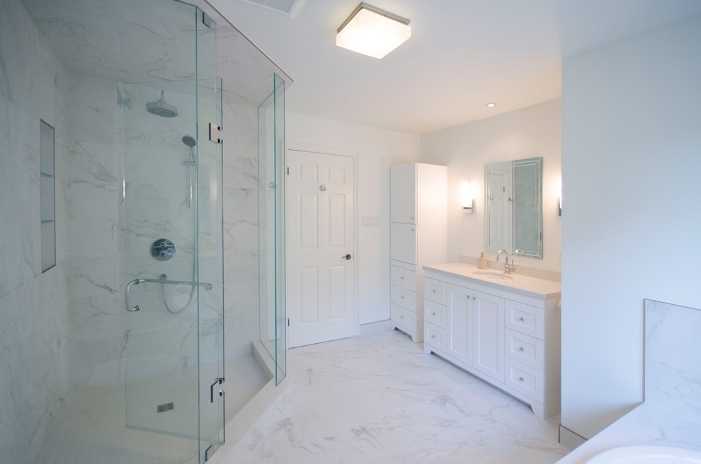 This is an example of a mid-sized transitional master bathroom in Toronto with shaker cabinets, white cabinets, a drop-in tub, a corner shower, a two-piece toilet, white tile, porcelain tile, white walls, porcelain floors, an undermount sink, engineered quartz benchtops, white floor and a hinged shower door.