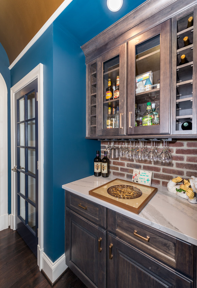 Photo of a traditional single-wall home bar in Richmond with no sink, glass-front cabinets, dark wood cabinets, brick splashback, dark hardwood floors, brown floor and white benchtop.