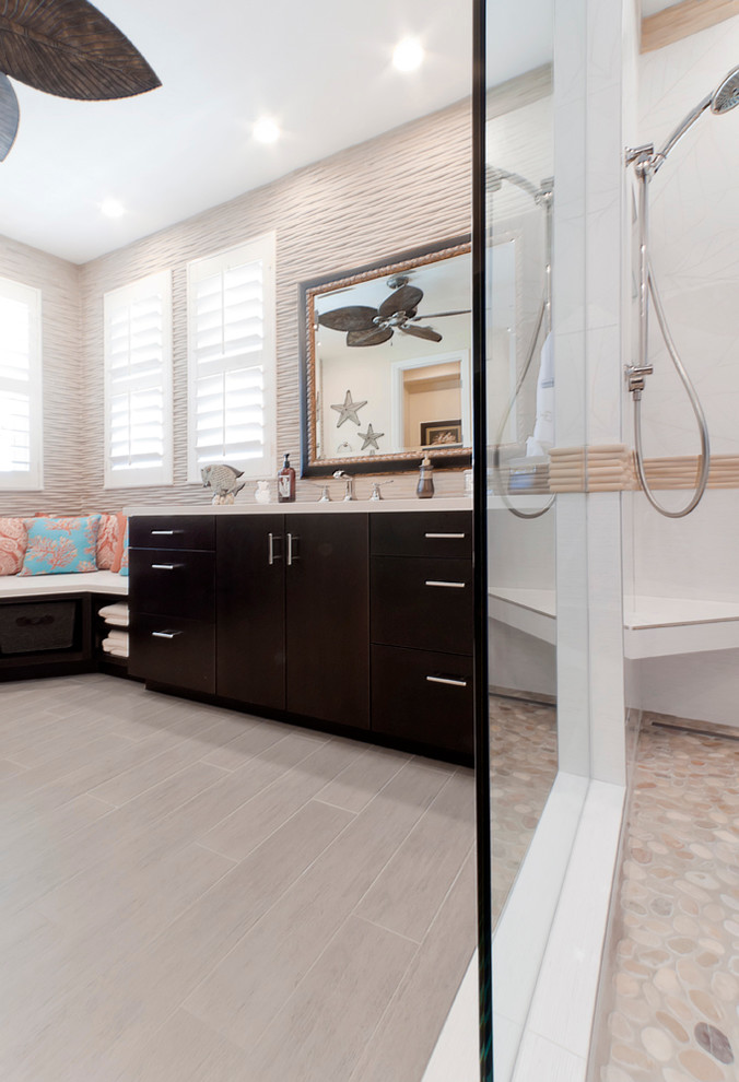 This is an example of an expansive beach style master bathroom in San Diego with flat-panel cabinets, dark wood cabinets, a corner shower, beige tile, stone tile, beige walls, light hardwood floors, an integrated sink and granite benchtops.