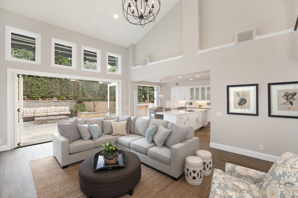Inspiration for a mid-sized transitional open concept family room in Orange County with grey walls, medium hardwood floors, a standard fireplace, a wall-mounted tv, brown floor, vaulted and a tile fireplace surround.