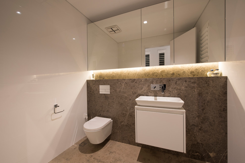 This is an example of a large modern powder room in Perth with white cabinets, a wall-mount toilet, multi-coloured tile, stone tile, white walls, slate floors and solid surface benchtops.