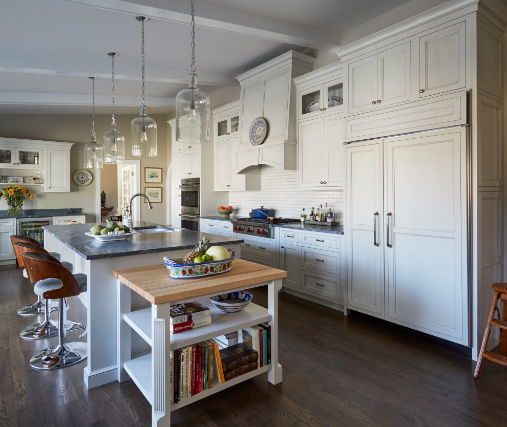 This is an example of a large traditional separate kitchen in Chicago with an undermount sink, recessed-panel cabinets, white cabinets, soapstone benchtops, white splashback, ceramic splashback, stainless steel appliances, medium hardwood floors, with island, brown floor, black benchtop and vaulted.