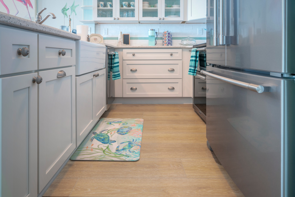 Photo of a small beach style galley separate kitchen in Wilmington with a farmhouse sink, shaker cabinets, white cabinets, stainless steel appliances, vinyl floors, yellow floor and a peninsula.