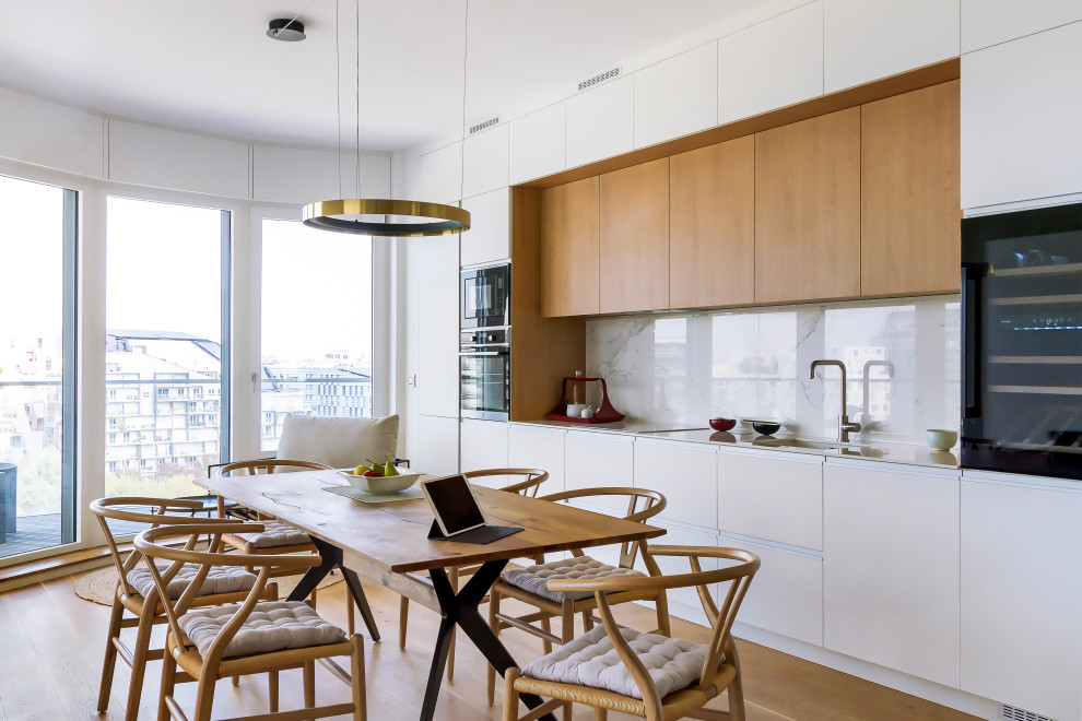 Inspiration for a contemporary single-wall eat-in kitchen in Paris with an undermount sink, flat-panel cabinets, white cabinets, white splashback, black appliances, medium hardwood floors, no island and brown floor.