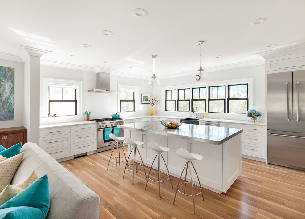 Inspiration for a transitional l-shaped kitchen in New York with a farmhouse sink, shaker cabinets, white cabinets, white splashback, stainless steel appliances, medium hardwood floors and with island.