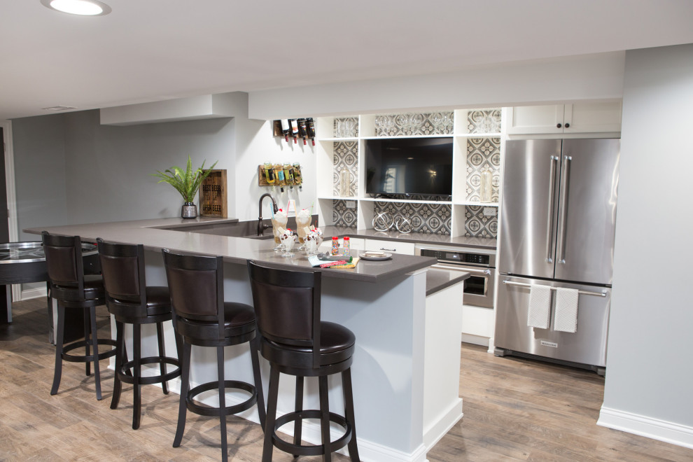 This is an example of a large transitional u-shaped wet bar in Chicago with an undermount sink, shaker cabinets, white cabinets, quartzite benchtops, multi-coloured splashback, porcelain splashback, vinyl floors, brown floor and grey benchtop.