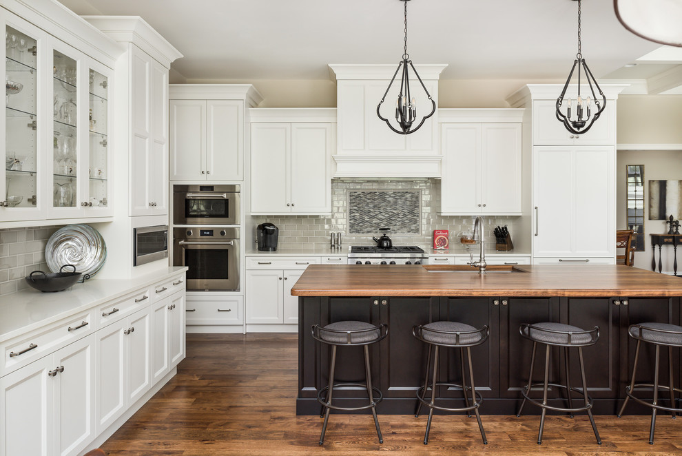 Inspiration for an expansive traditional open plan kitchen in Chicago with an undermount sink, shaker cabinets, white cabinets, quartz benchtops, grey splashback, dark hardwood floors, with island, brown floor, white benchtop, subway tile splashback and stainless steel appliances.