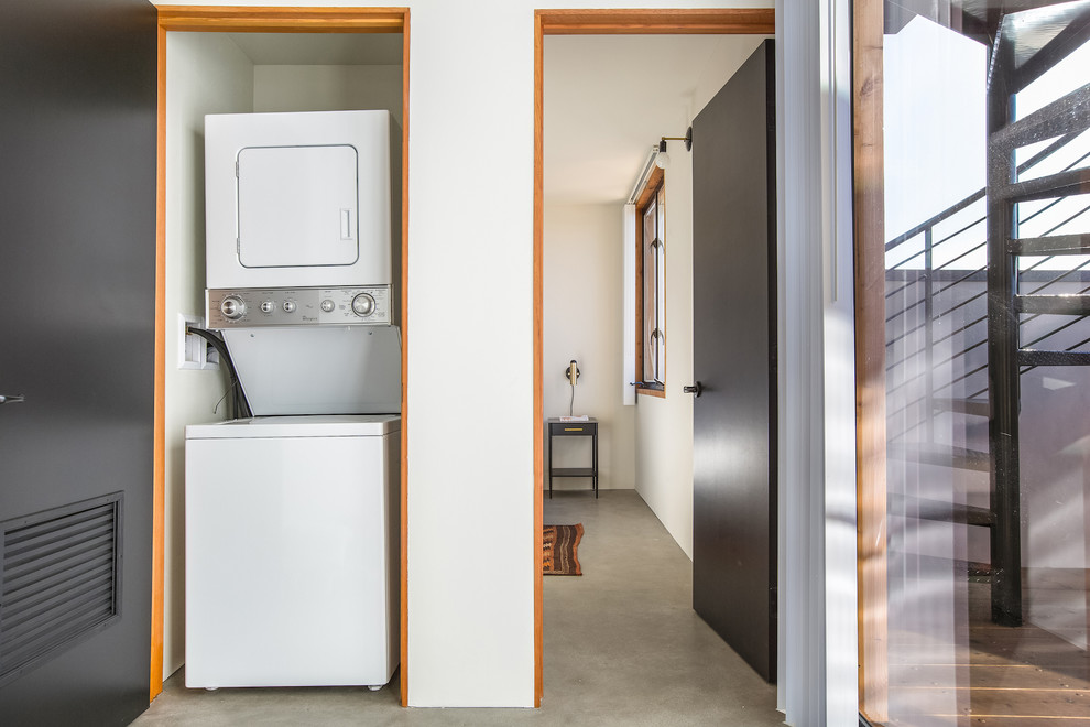 Inspiration for a midcentury laundry room in Miami with concrete floors, a stacked washer and dryer and grey floor.