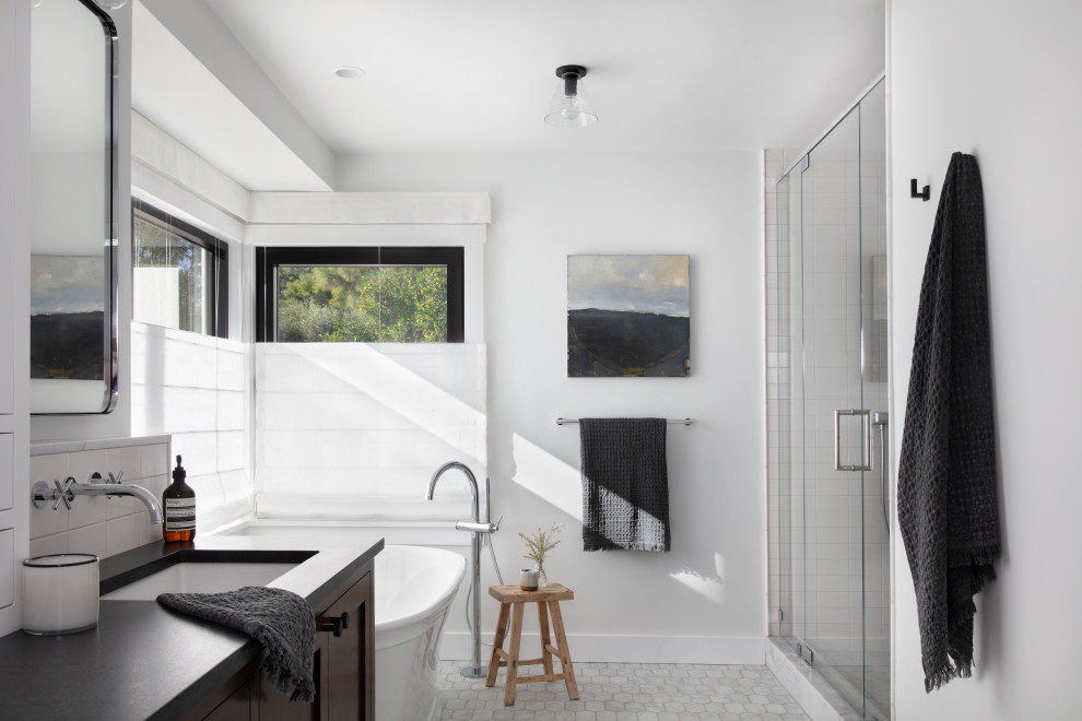 Inspiration for a mid-sized country master bathroom in Santa Barbara with recessed-panel cabinets, dark wood cabinets, a freestanding tub, an alcove shower, white walls, ceramic floors, an undermount sink, solid surface benchtops, white floor, a hinged shower door, black benchtops, a double vanity and a built-in vanity.