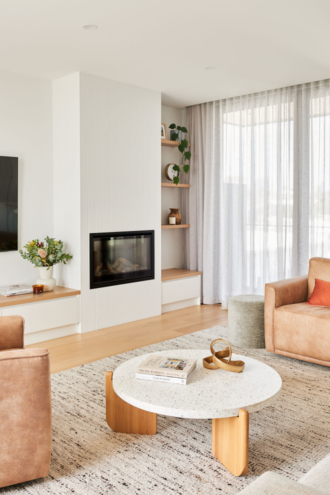 Large beach style open concept living room in Geelong with white walls, light hardwood floors, a standard fireplace, a wood fireplace surround, a wall-mounted tv and brown floor.