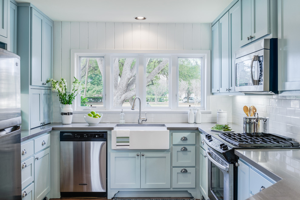 Inspiration for a traditional u-shaped kitchen in Austin with a farmhouse sink, shaker cabinets, blue cabinets, stainless steel appliances, no island, white splashback, subway tile splashback and solid surface benchtops.