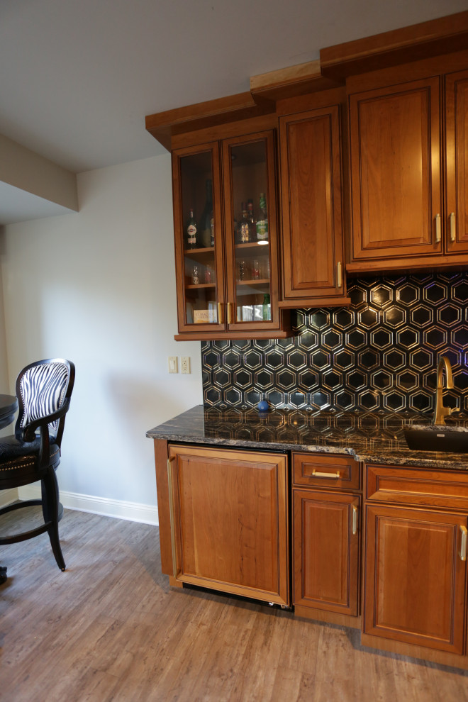Mid-sized traditional single-wall wet bar in Baltimore with an undermount sink, raised-panel cabinets, medium wood cabinets, granite benchtops, black splashback, marble splashback, plywood floors, beige floor and black benchtop.