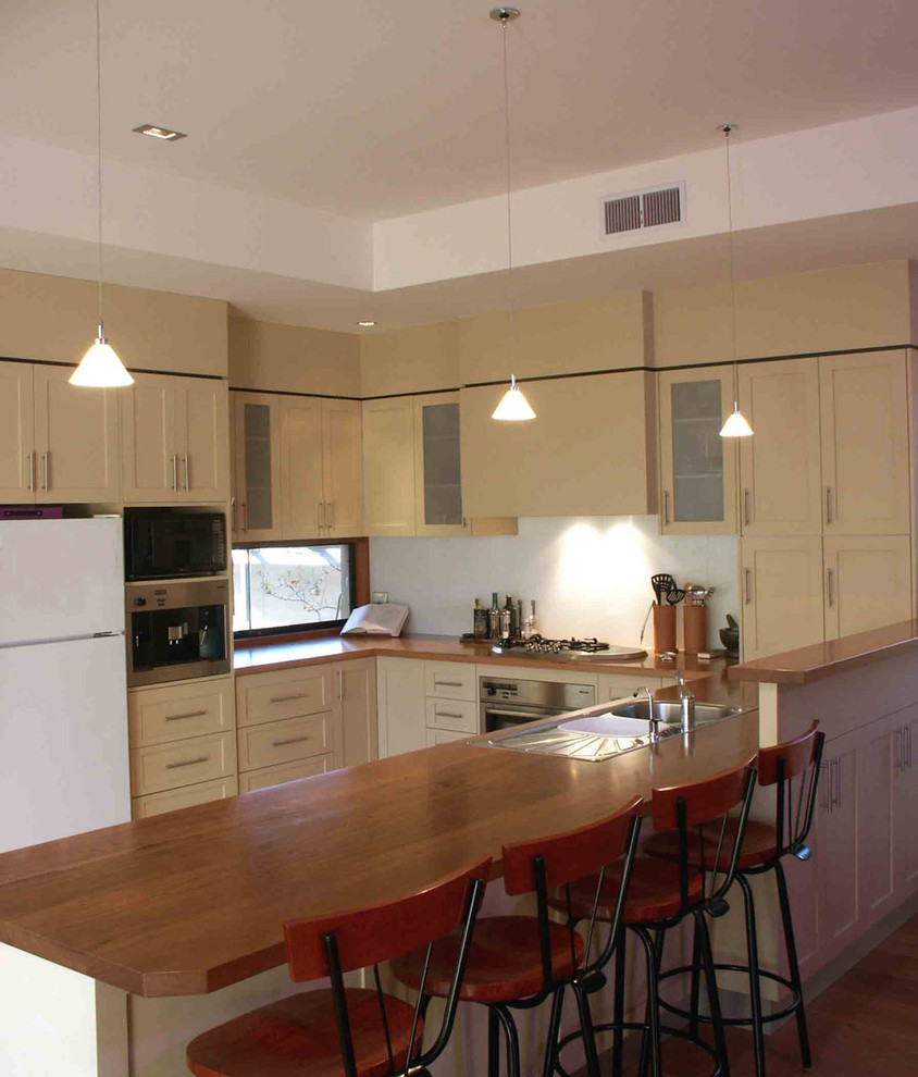 Inspiration for a mid-sized transitional u-shaped open plan kitchen in Geelong with a double-bowl sink, shaker cabinets, beige cabinets, wood benchtops, white splashback, glass sheet splashback, stainless steel appliances, medium hardwood floors and a peninsula.