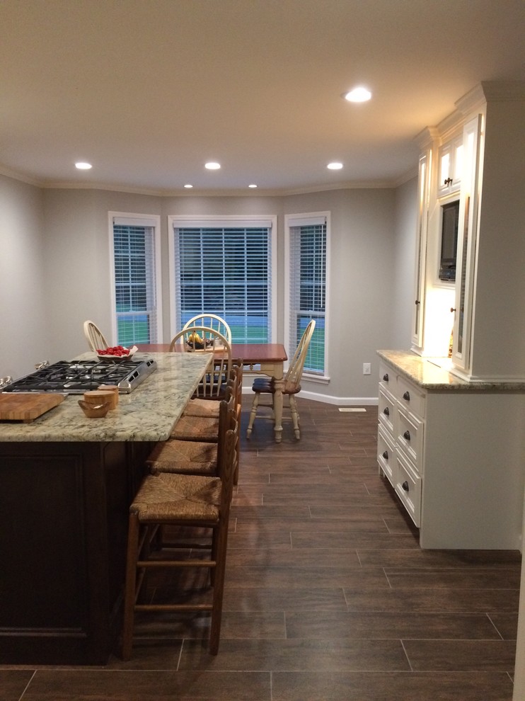 Example of a large transitional l-shaped brown floor eat-in kitchen design in Birmingham with a farmhouse sink, recessed-panel cabinets, white cabinets, beige backsplash, stainless steel appliances and an island