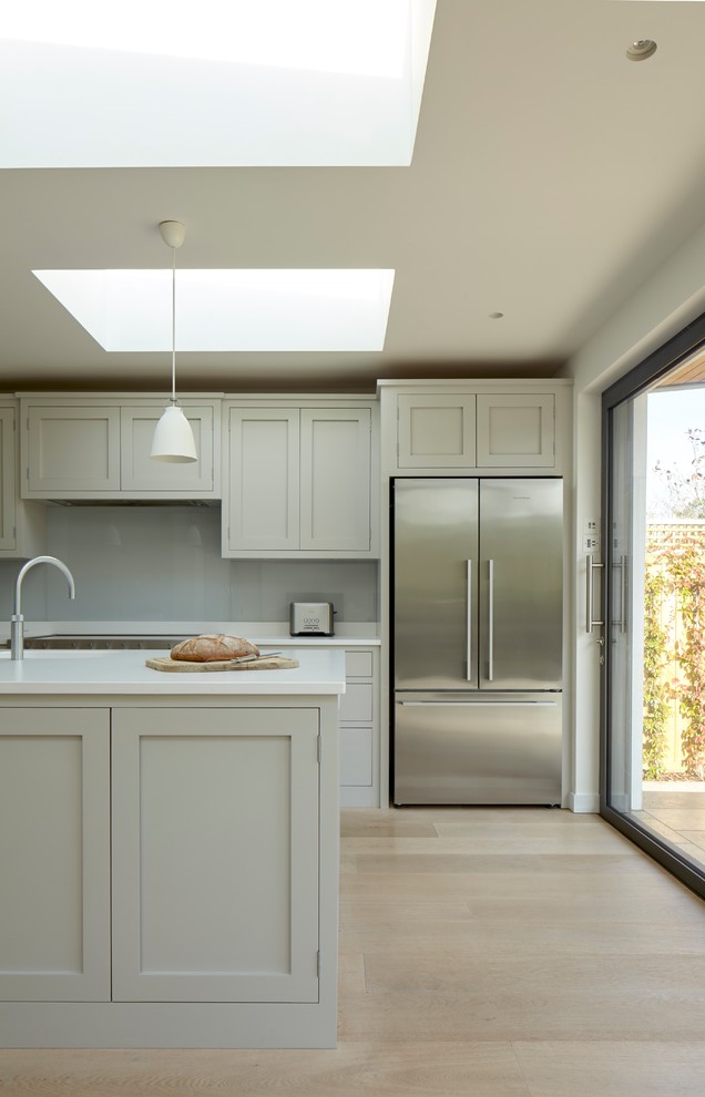 Design ideas for a mid-sized contemporary single-wall open plan kitchen in Surrey with an integrated sink, shaker cabinets, grey cabinets, quartz benchtops, white splashback, glass sheet splashback, stainless steel appliances, light hardwood floors, with island and beige floor.