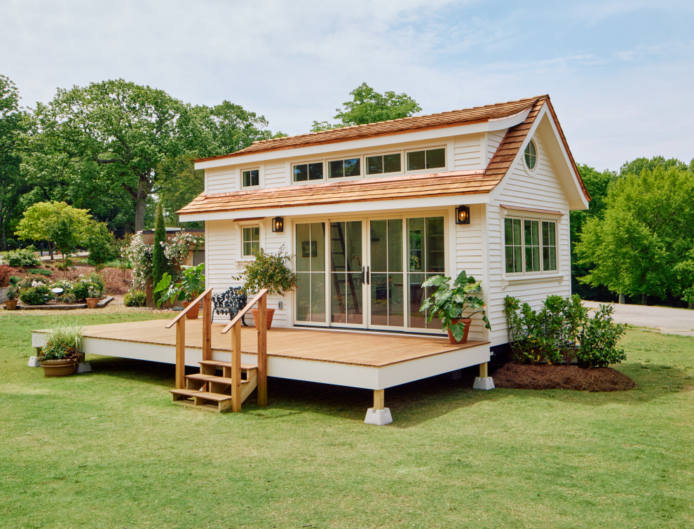 Esempio della micro casa piccola bianca con rivestimento con lastre in cemento, tetto a capanna, copertura a scandole, tetto marrone e pannelli sovrapposti