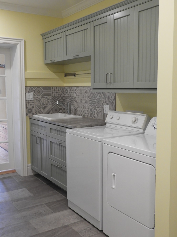 Photo of a small country galley utility room in Toronto with a drop-in sink, beaded inset cabinets, green cabinets, laminate benchtops, yellow walls, vinyl floors, a side-by-side washer and dryer, grey floor and grey benchtop.