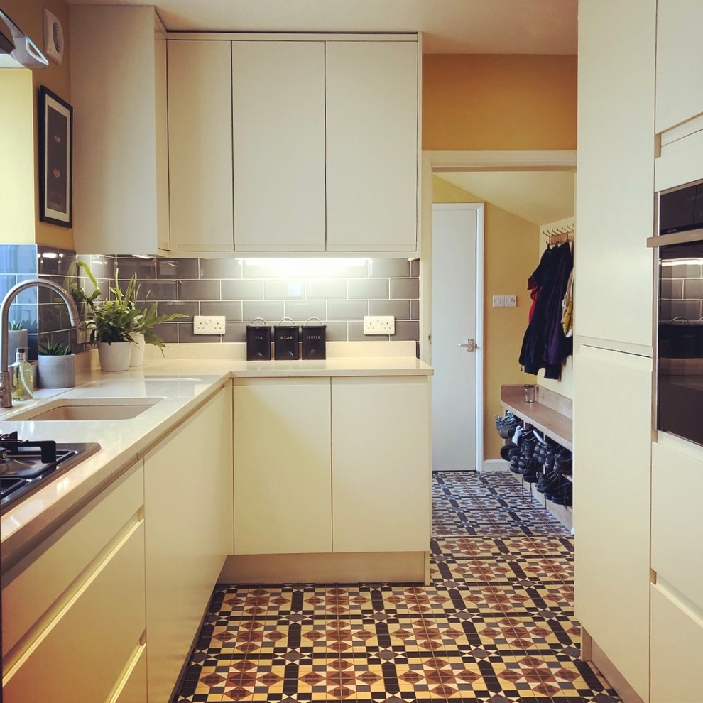 This is an example of a mid-sized traditional galley separate kitchen in Other with an undermount sink, flat-panel cabinets, beige cabinets, solid surface benchtops, blue splashback, ceramic splashback, stainless steel appliances, ceramic floors, no island, multi-coloured floor and beige benchtop.