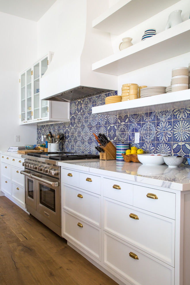 Photo of a large transitional single-wall open plan kitchen in Los Angeles with a farmhouse sink, recessed-panel cabinets, white cabinets, marble benchtops, grey splashback, ceramic splashback, panelled appliances, light hardwood floors, with island and brown floor.