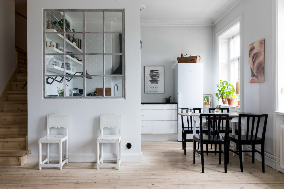 Small scandinavian u-shaped eat-in kitchen in New York with flat-panel cabinets, white cabinets, white appliances, light hardwood floors, no island, beige floor and black benchtop.