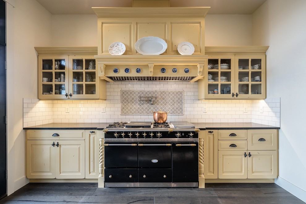 Design ideas for a large transitional l-shaped open plan kitchen in Seattle with a farmhouse sink, raised-panel cabinets, yellow cabinets, soapstone benchtops, white splashback, subway tile splashback, black appliances, medium hardwood floors, with island, brown floor and grey benchtop.